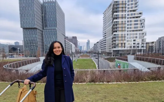 Woman standing in-between two tall skyscrapers with her hand on the stroller handle.