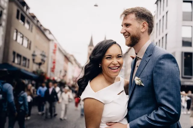 Man in a blue suit and woman in white dress on their wedding day. Both are smiling.
