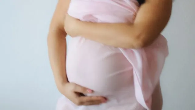 Pregnant woman holding her stomach, wearing a light pink transparent cover-up.