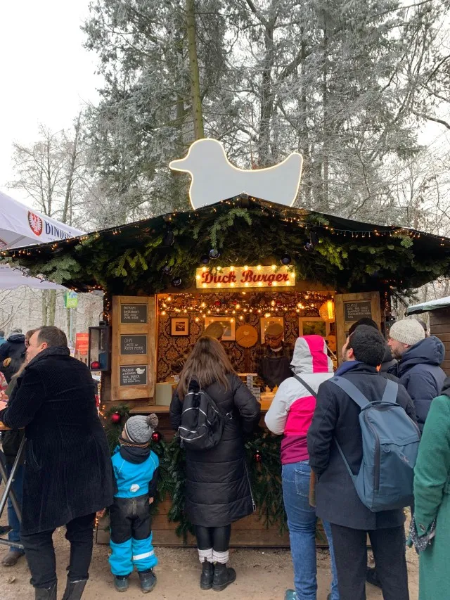 A small crowd of people patiently waiting in life in front of a Christmas market stand in Frankfurt, Germany.