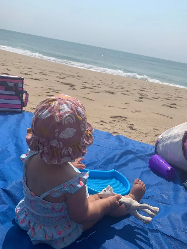 Niña pequeña sentada en la arena mirando al océano, de espaldas a la cámara.