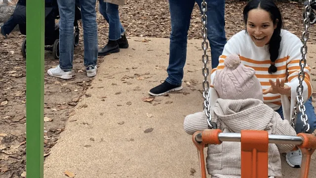 Mother pushing daughter on the swing. She is smiling and happy.