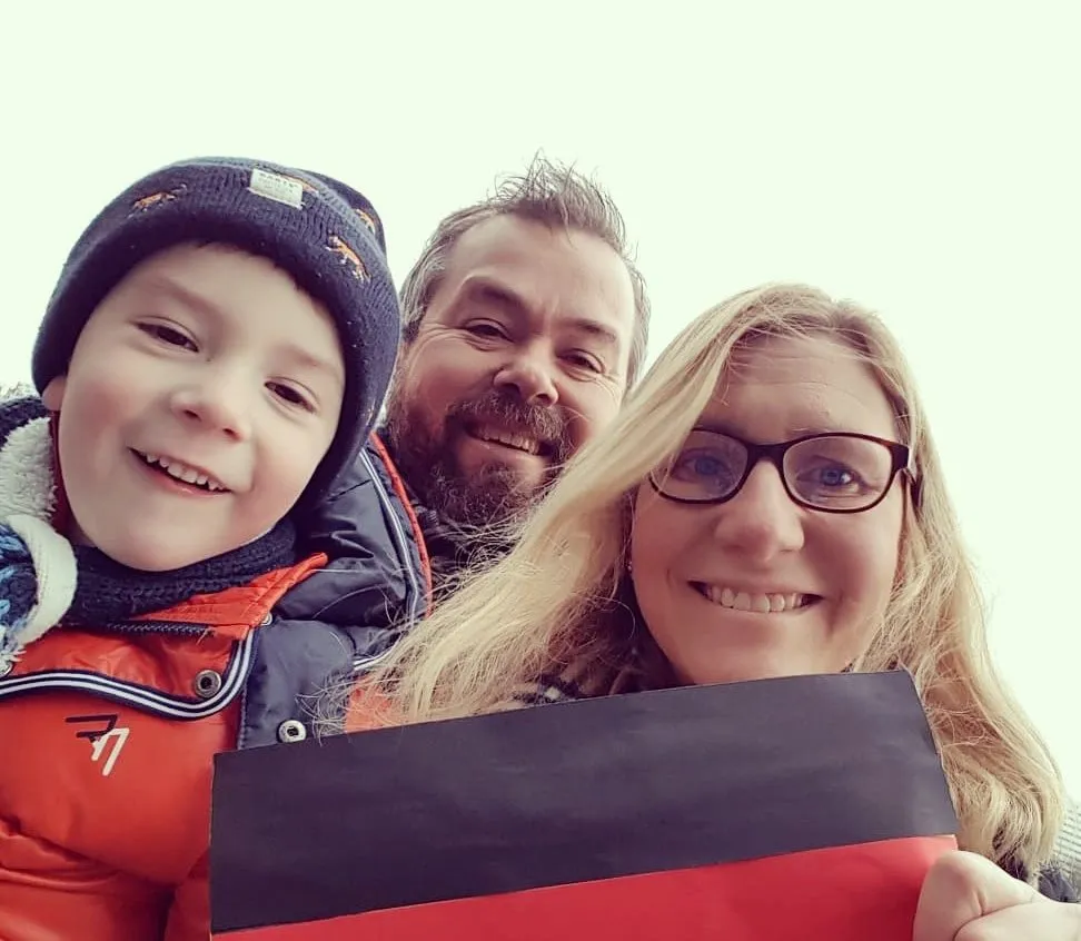 A family of 3 including husband, wife, and small son. Mother is holding a German flag as the family celebrates becoming German citizens.