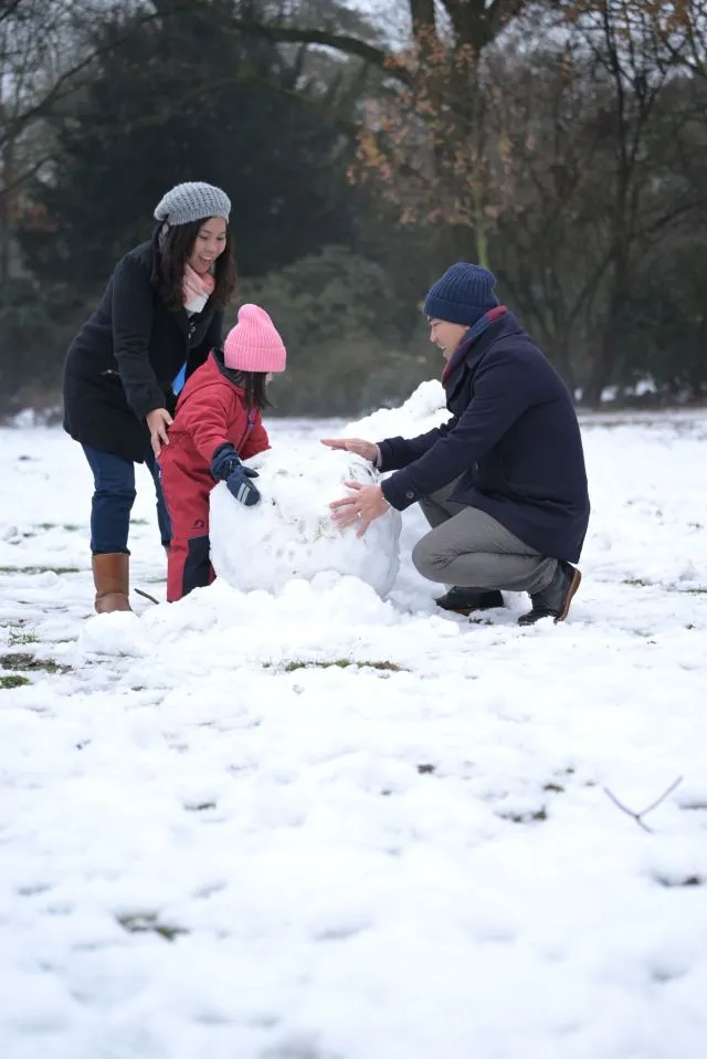 Mother, father and child happily building a snowman outside.